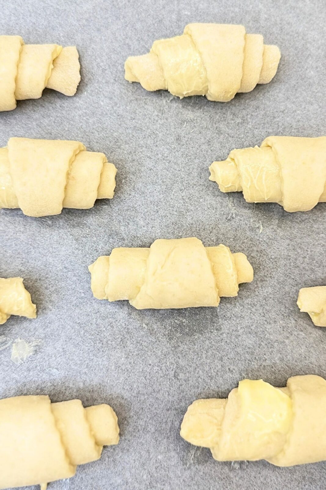 Unbaked homemade crescent rolls spaced apart on a parchment-lined baking sheet, ready to rise.