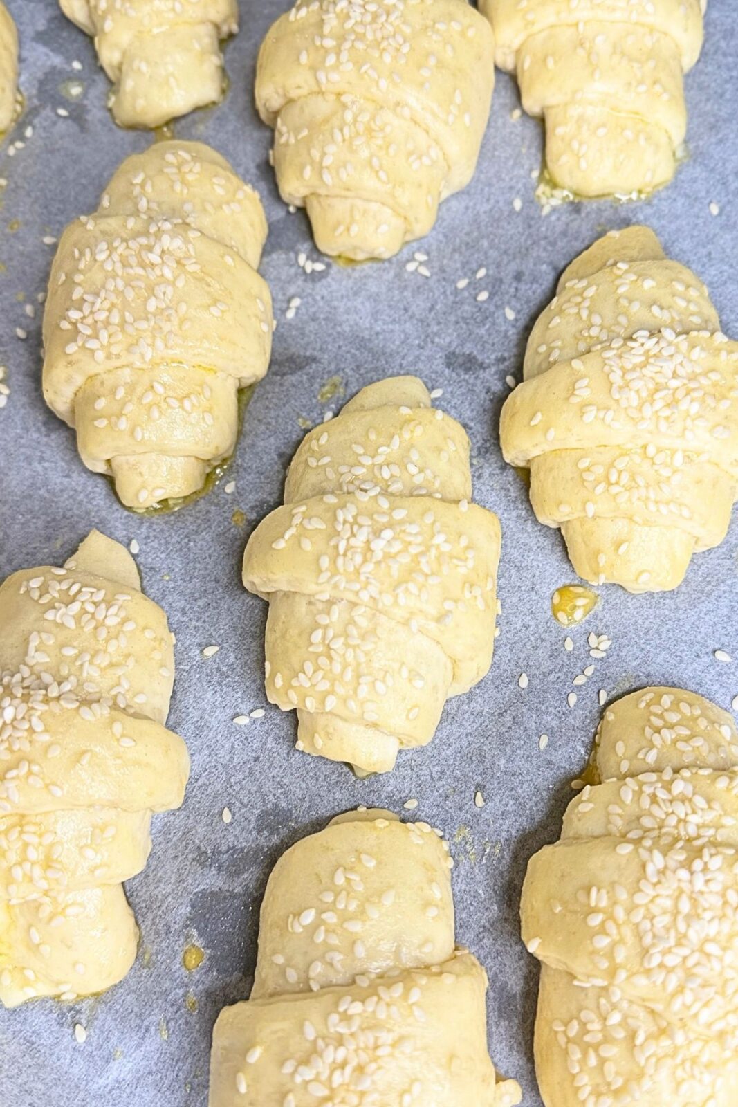 Unbaked crescent rolls brushed with egg wash and topped with sesame seeds on a parchment-lined baking sheet.