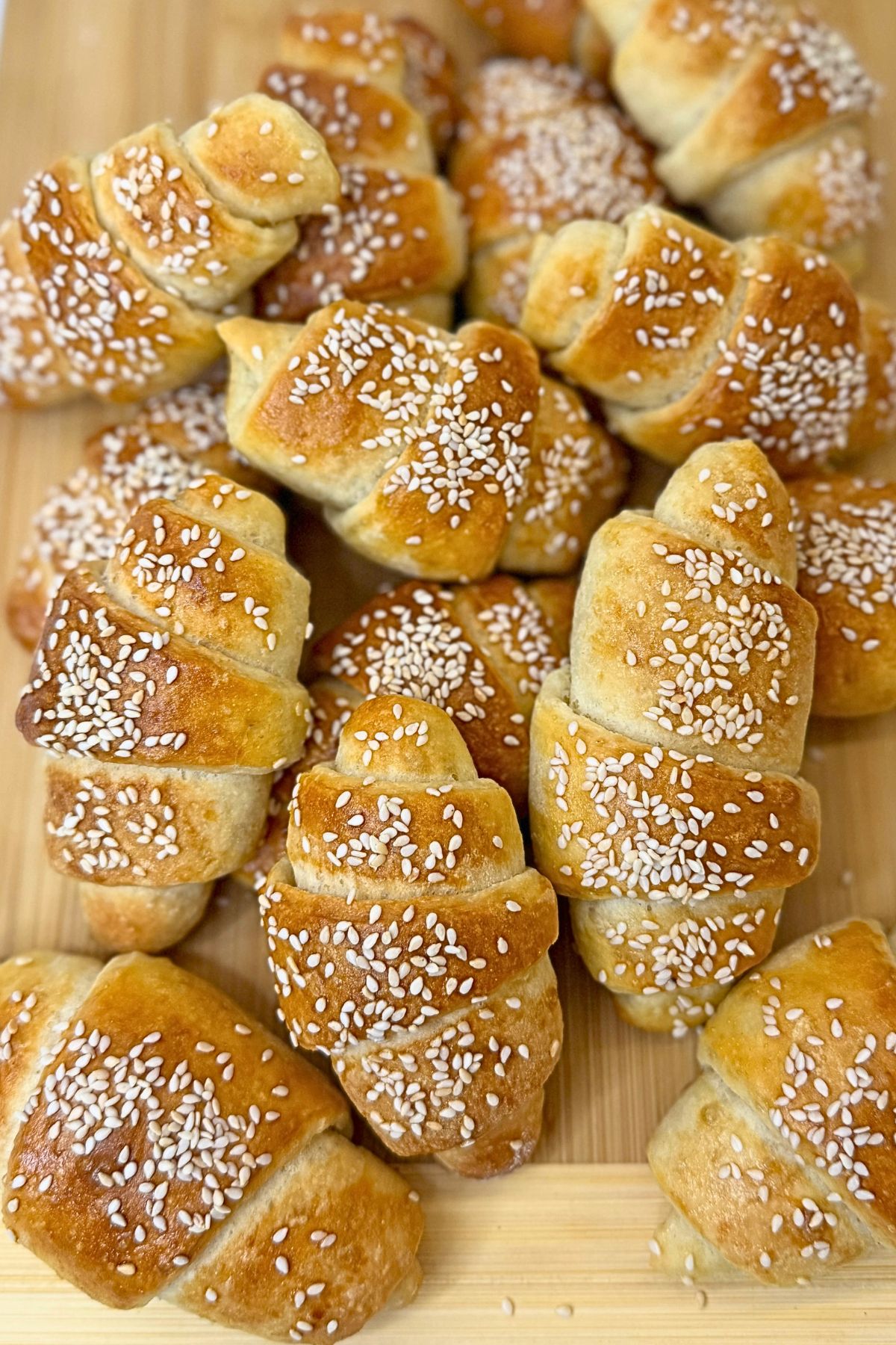 Homemade crescent rolls topped with sesame seeds on a light platter, with a split roll showing the soft, fluffy interior.
