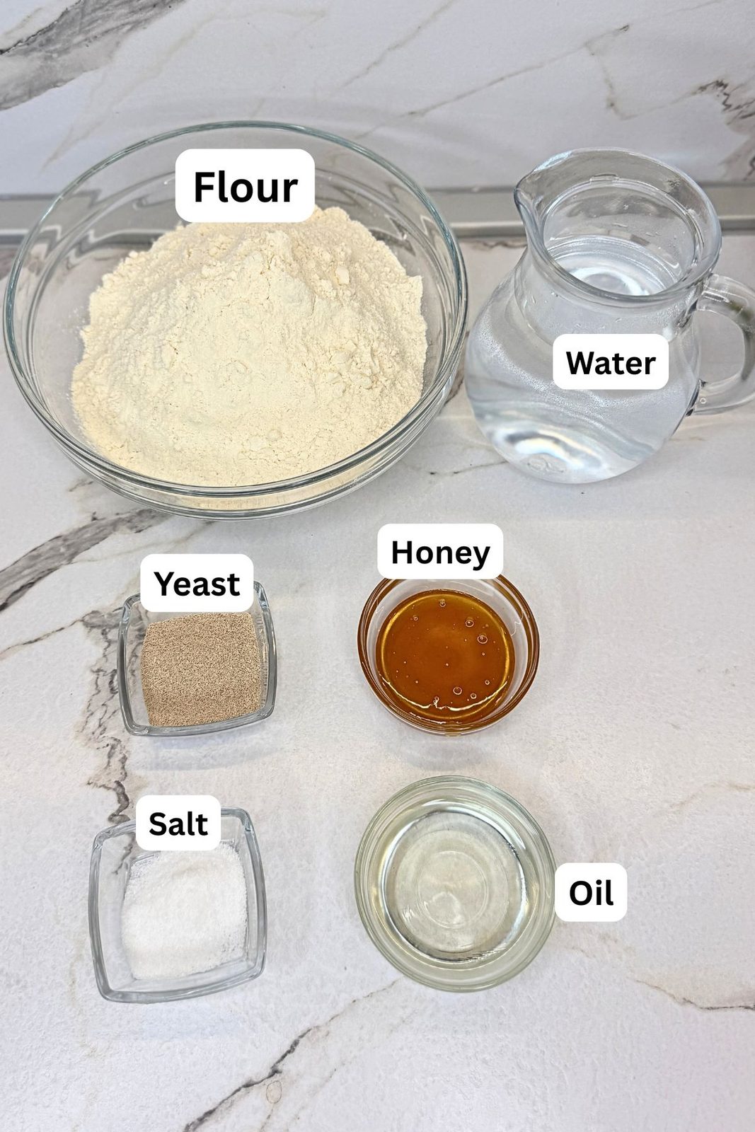 Ingredients for homemade sandwich bread in labeled containers: flour, water, yeast, honey, salt, and oil.