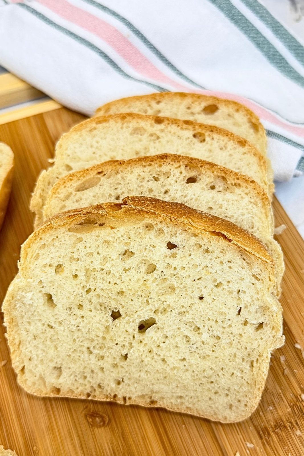 Slices of homemade sandwich bread arranged on a wooden cutting board, showing a soft, airy crumb and golden crust.