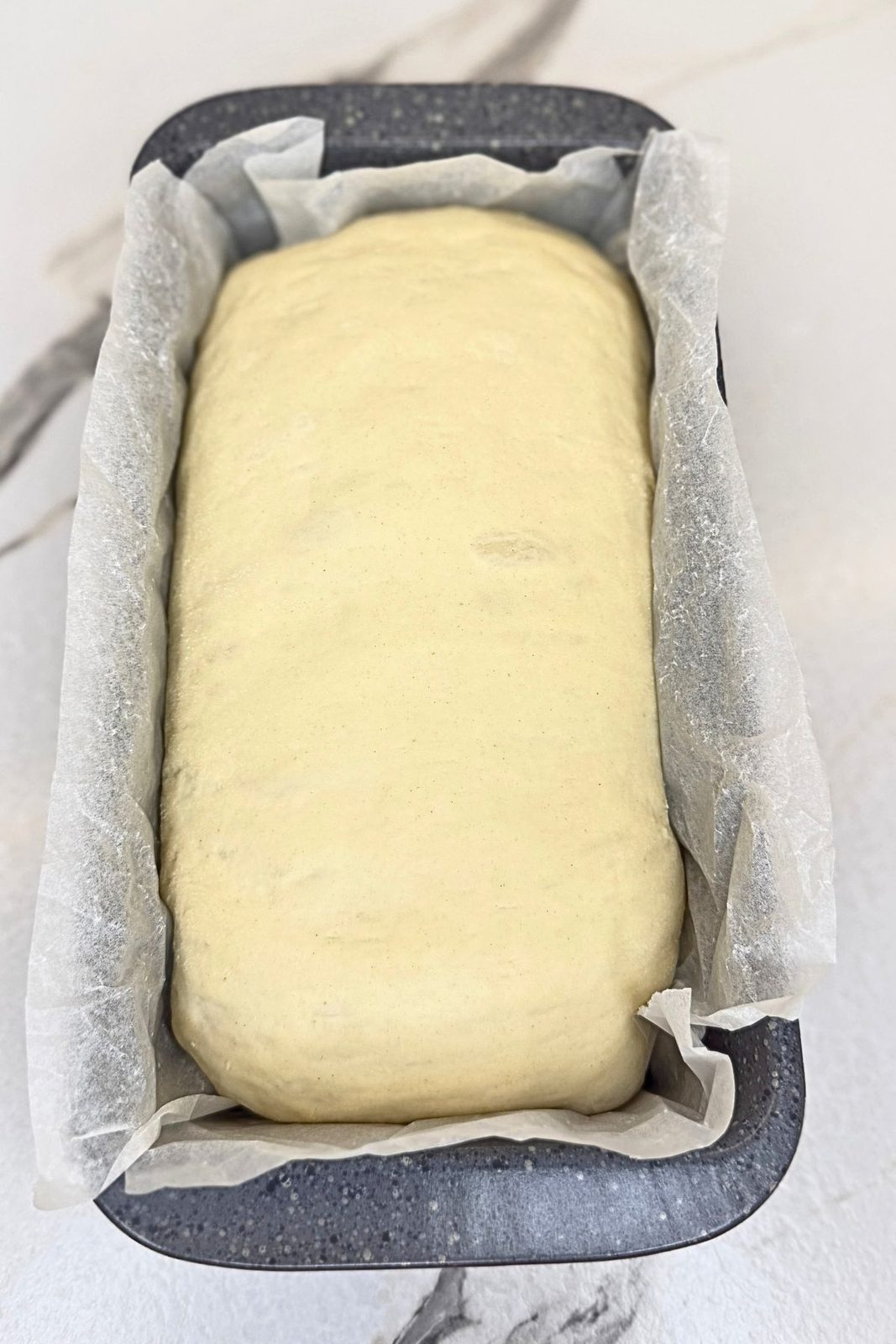 Puffy sandwich bread dough in a parchment-lined loaf pan, ready to bake.