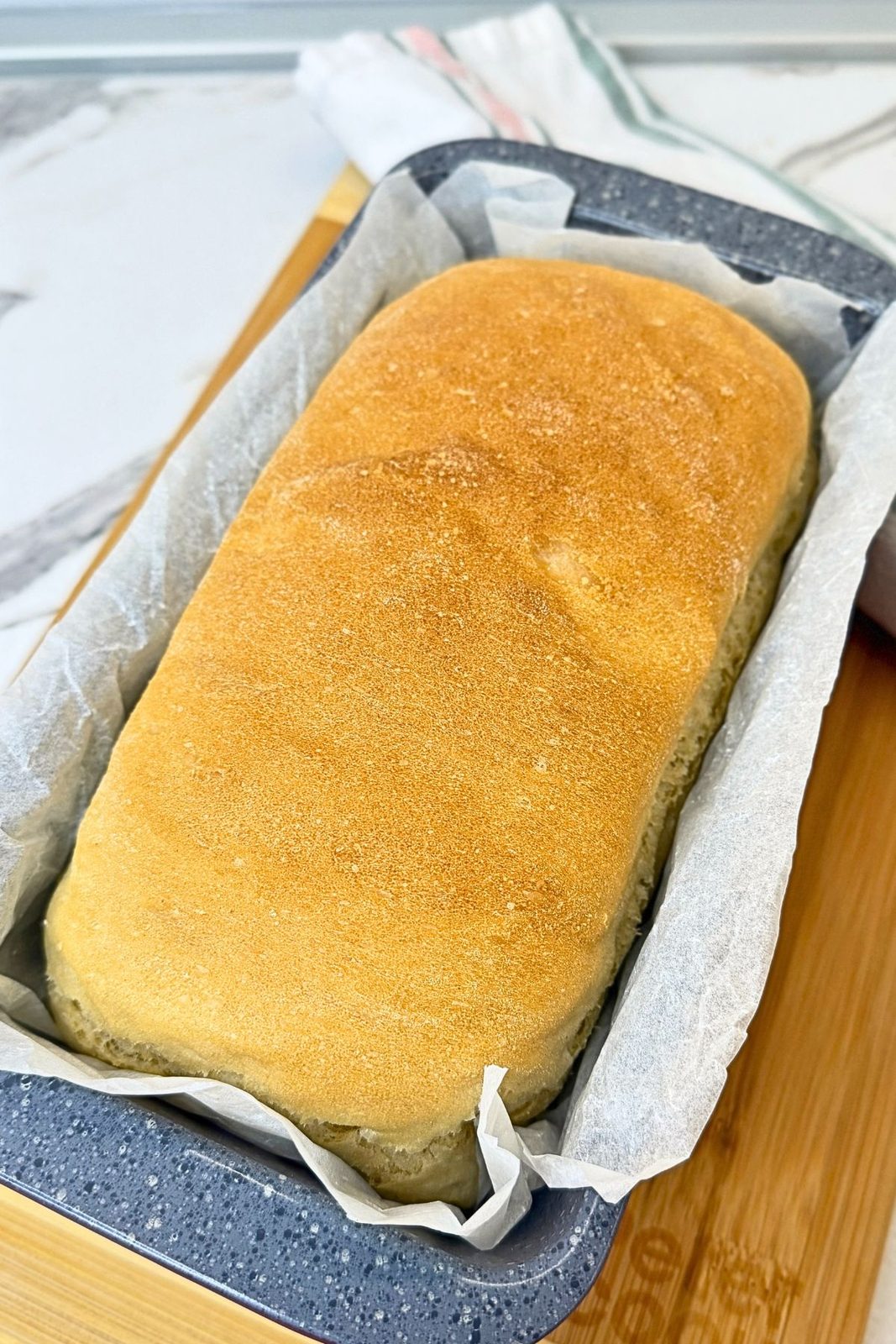 Freshly baked homemade sandwich bread with a golden crust in a parchment-lined loaf pan.