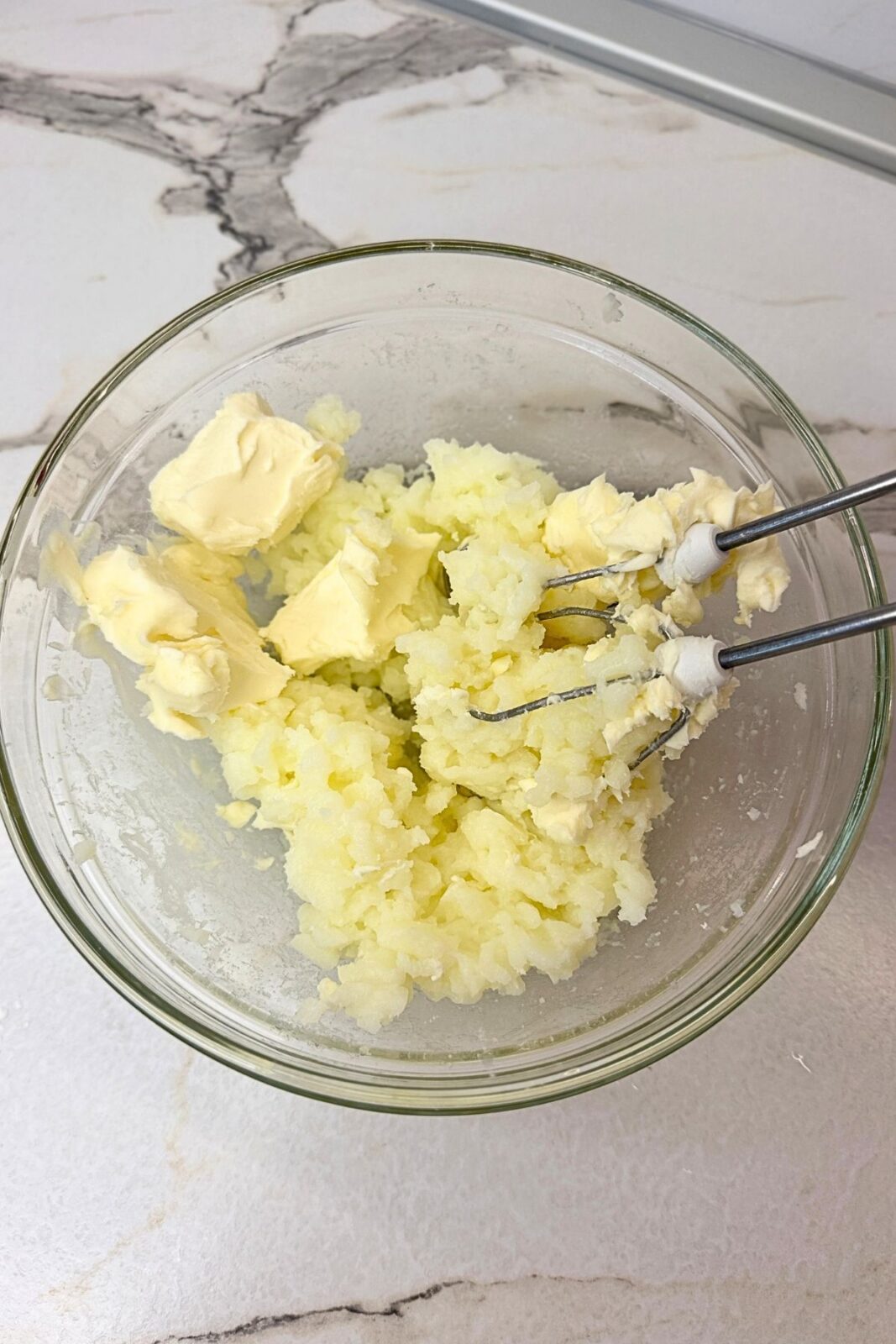 Softened butter being mixed into the cooled milk cream with an electric mixer.