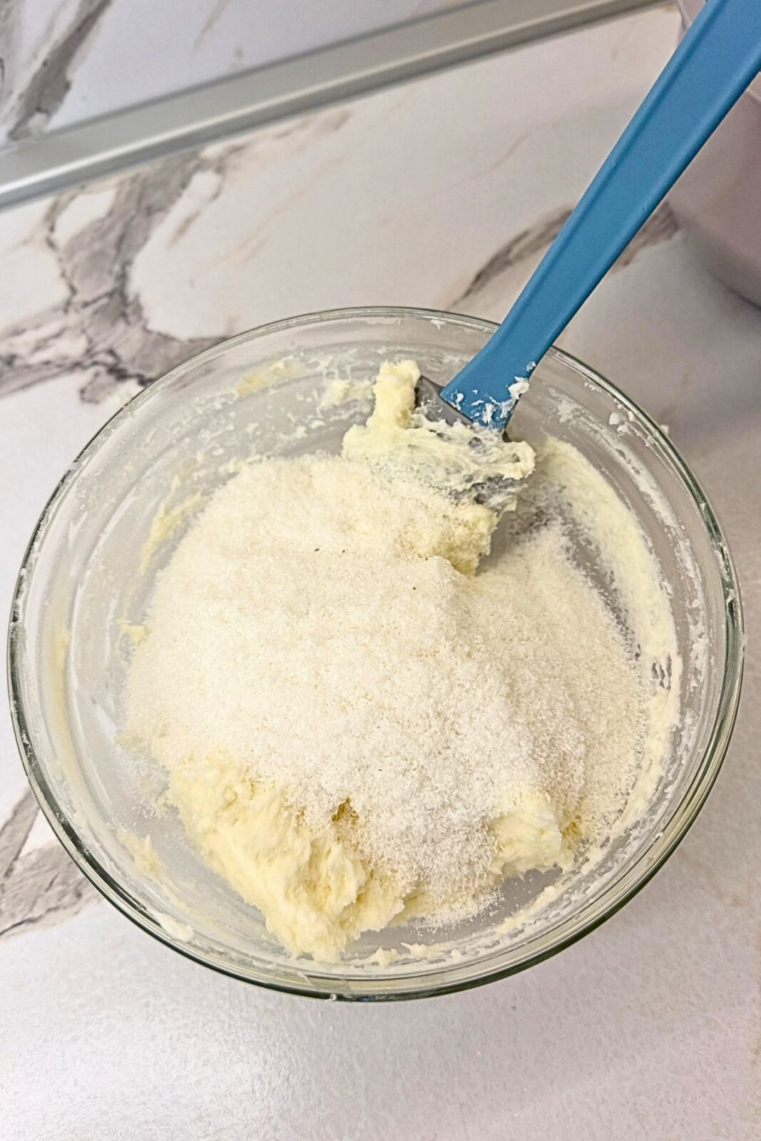 Desiccated coconut added to the creamy Raffaello filling in a glass mixing bowl.
