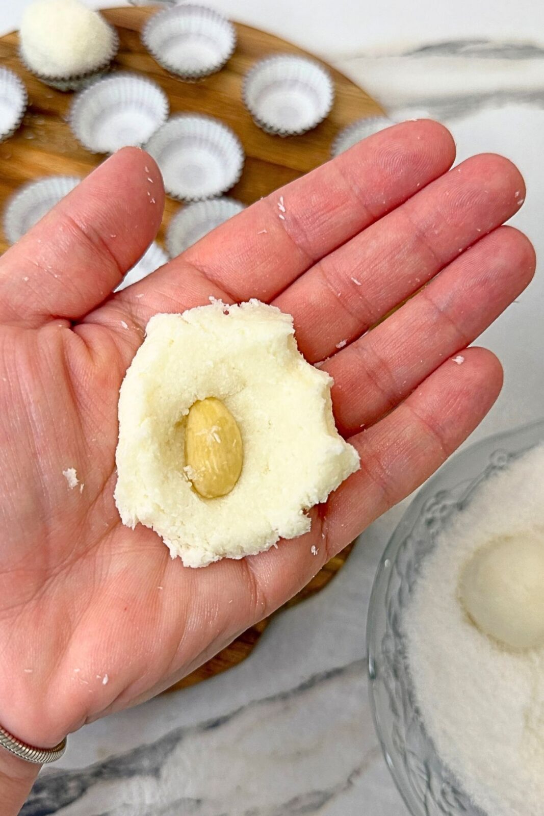 A whole blanched almond placed in the center of flattened coconut filling before shaping into a ball.
