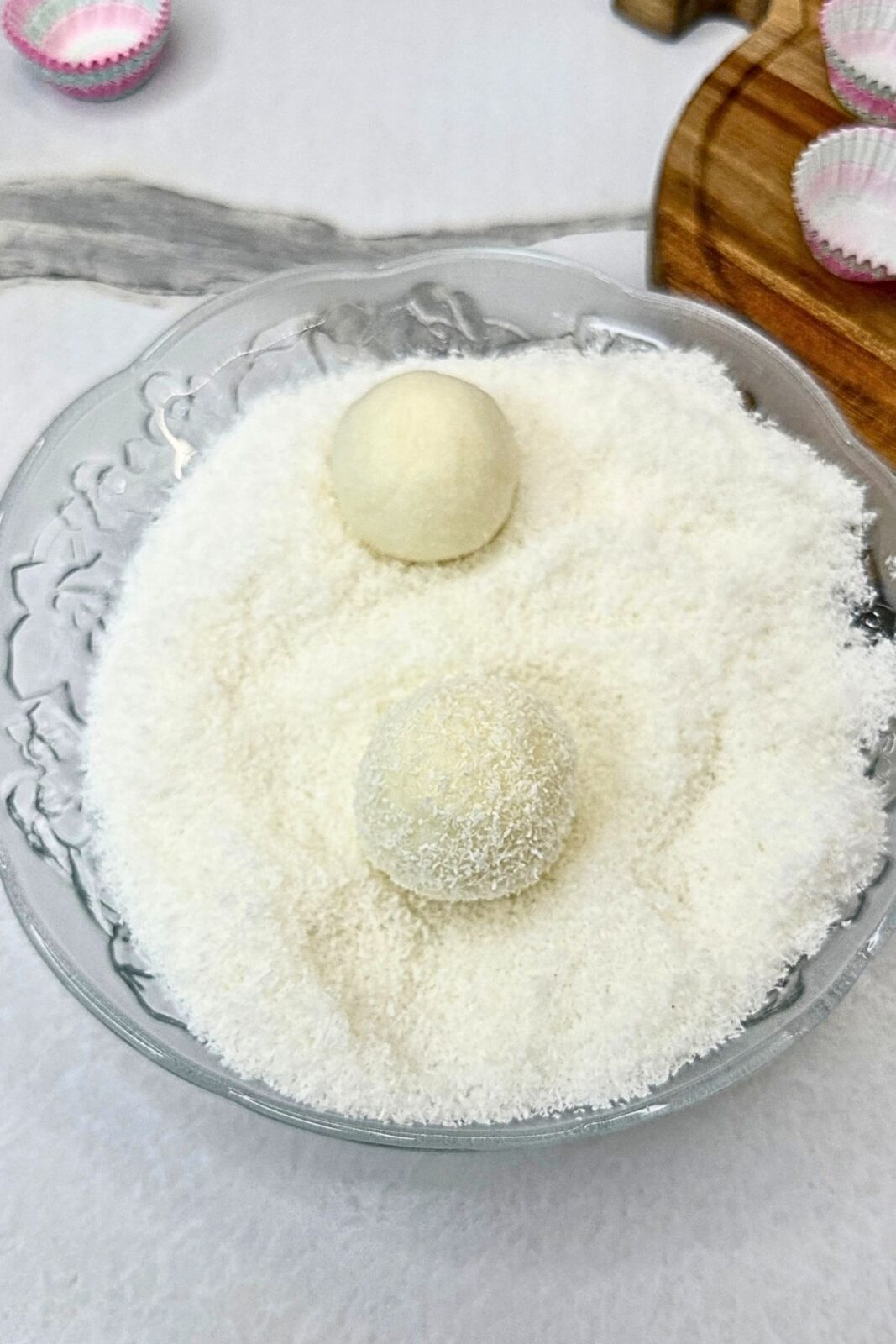 Raffaello coconut balls in a shallow bowl of desiccated coconut for coating.