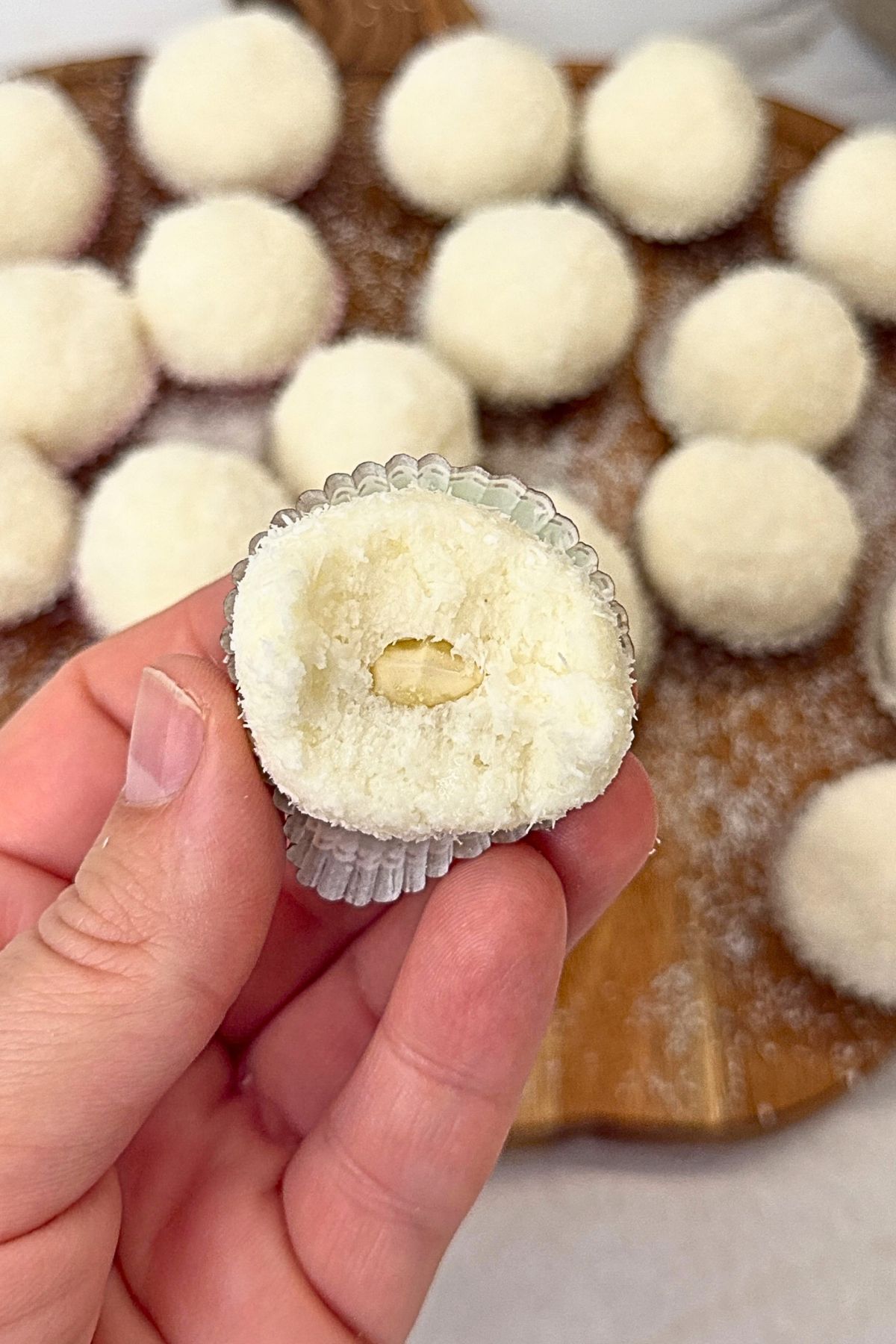 Homemade Raffaello coconut balls on a wooden board, with one split open to reveal the creamy coconut filling and almond center.