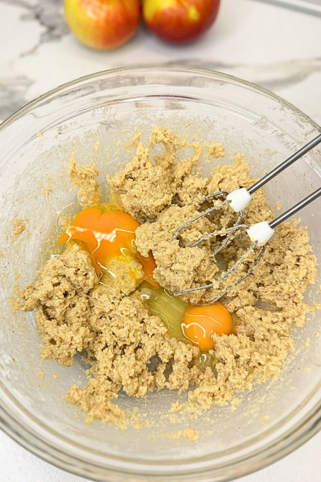 Eggs added to creamed butter and sugars in a glass bowl with electric mixer beaters.