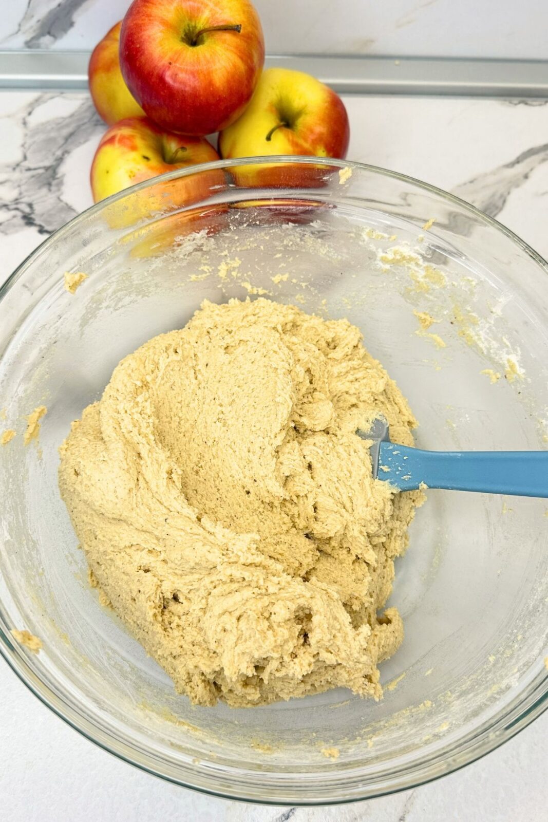 Cinnamon cookie dough in a glass mixing bowl with a blue spatula.