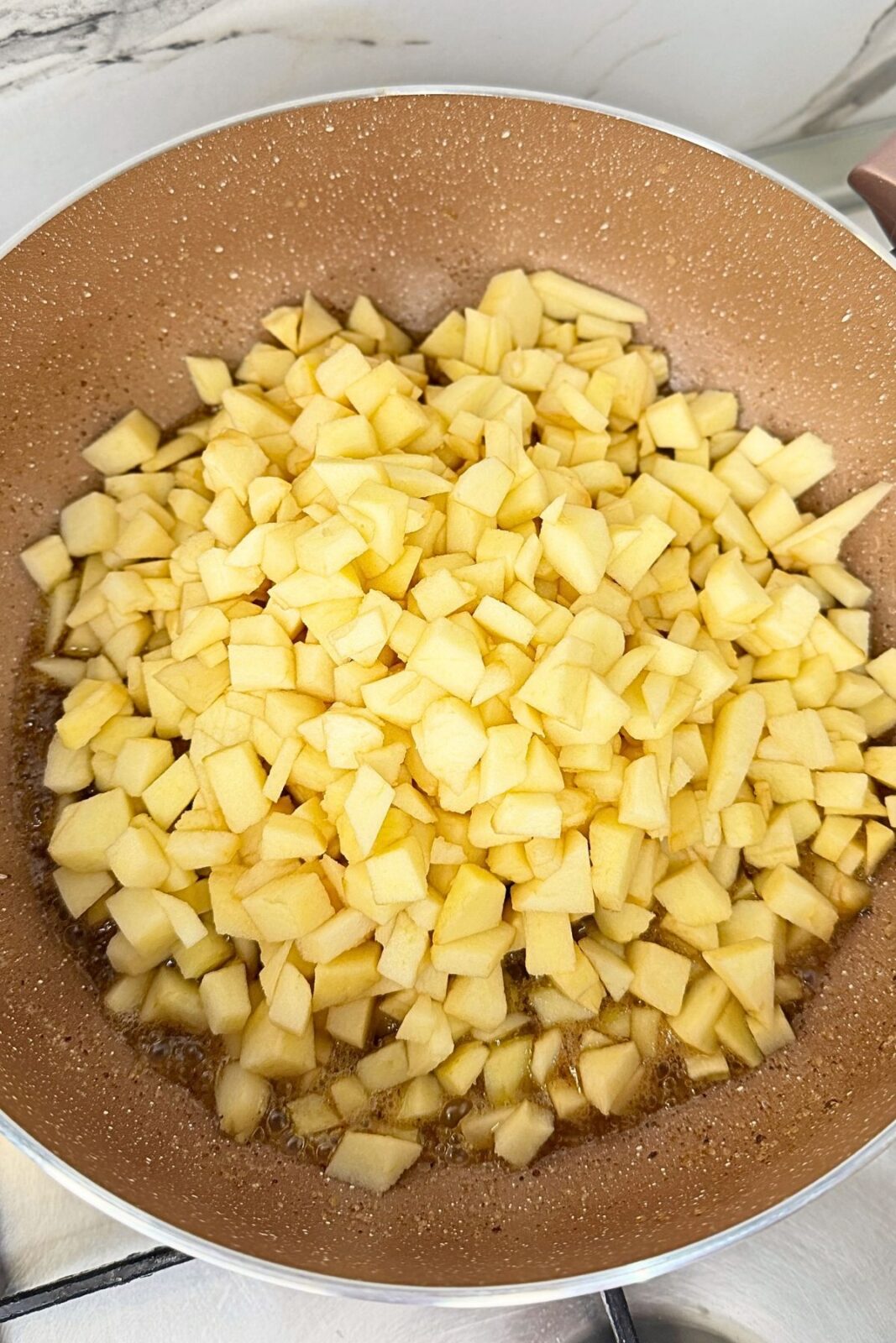 Diced peeled apples added to cinnamon butter in a skillet.