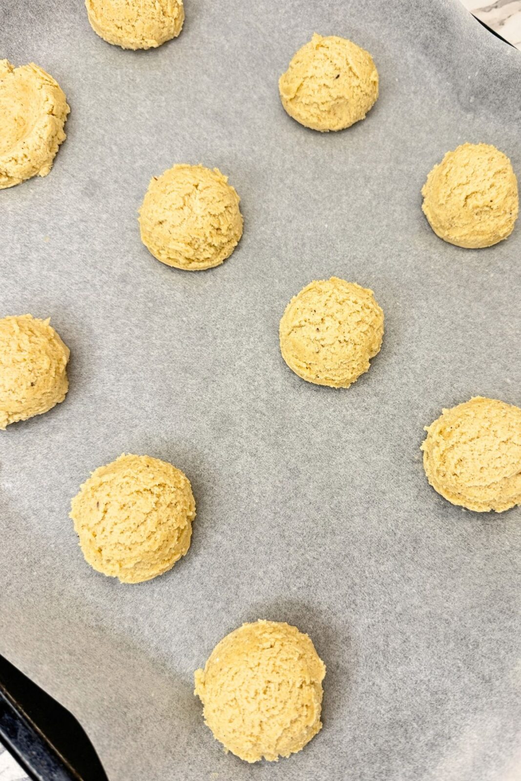 Portions of apple pie cookie dough spaced apart on a parchment-lined baking sheet.