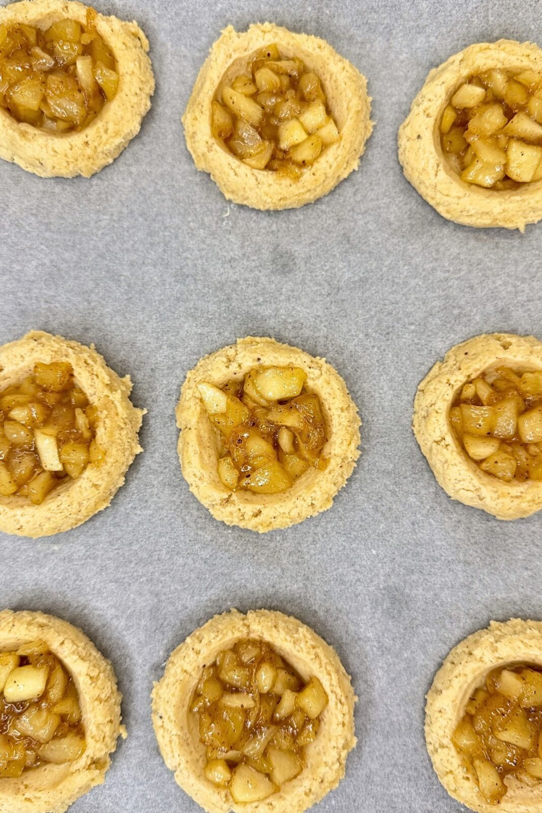 Unbaked apple pie cookies filled with cinnamon-spiced apples on parchment paper.