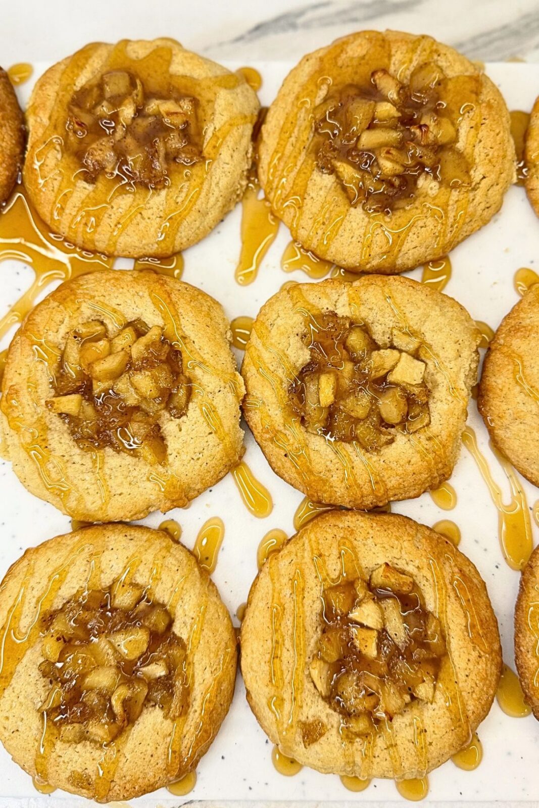 Apple pie cookies filled with cinnamon-spiced apples and drizzled with caramel sauce on a white serving platter.