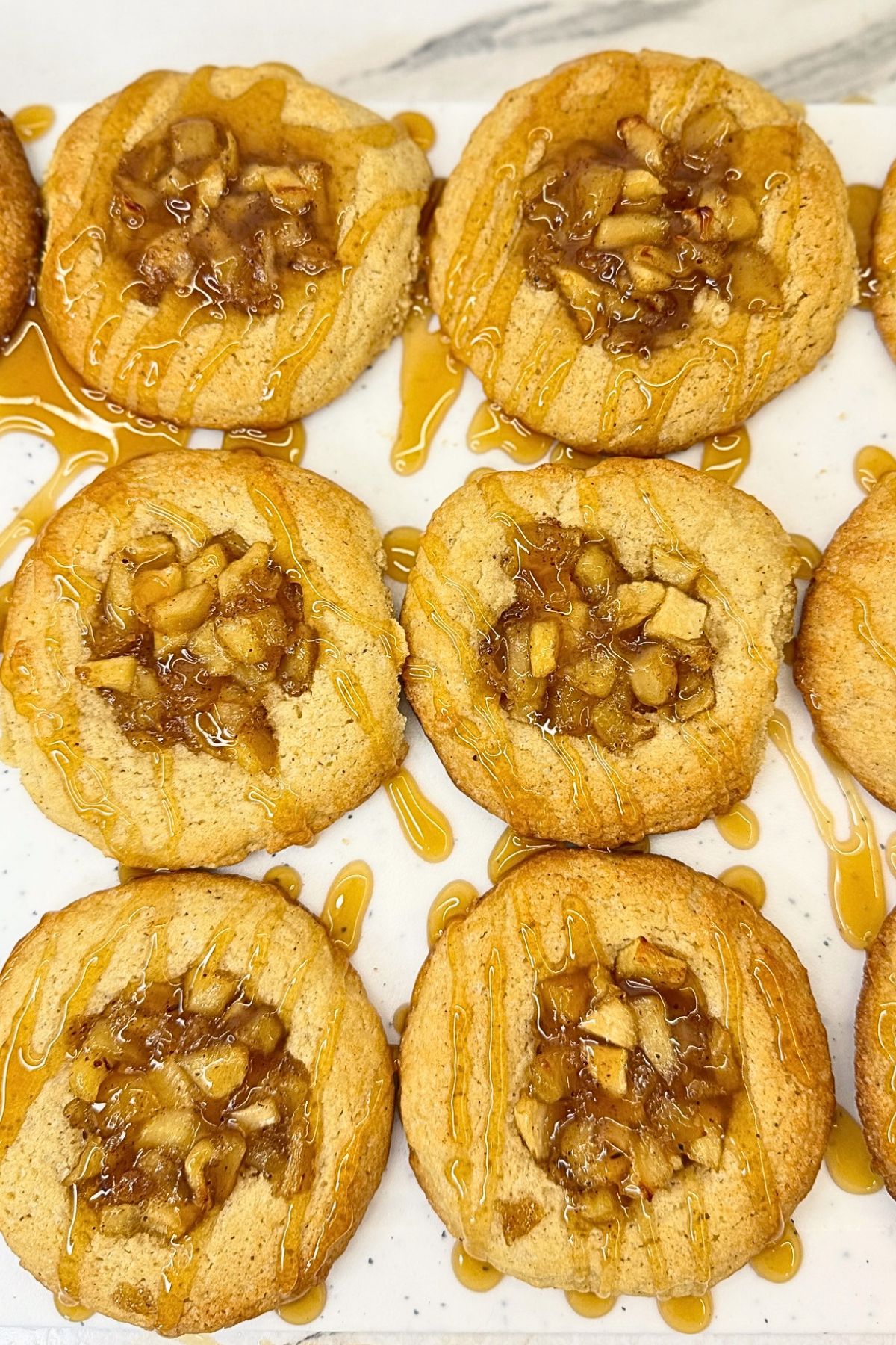 Apple pie cookies with cinnamon apple filling and caramel drizzle, with two cookie halves stacked on top to show the soft centers.