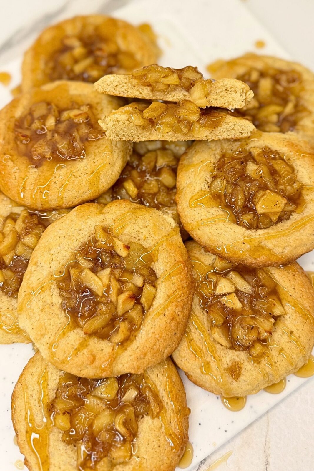 Apple pie cookies with cinnamon apple filling and caramel drizzle, topped with two stacked cookie halves showing the inside.