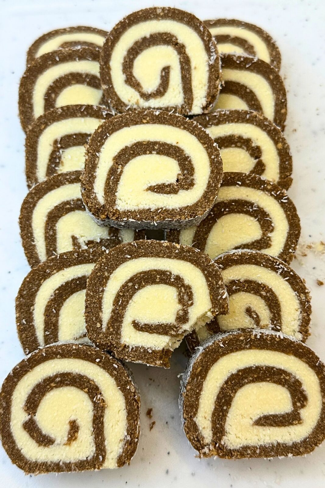 Chocolate coconut roll slices arranged on a white platter, with a slice in focus showing the cocoa cookie layer, coconut filling, and coconut-covered edge.