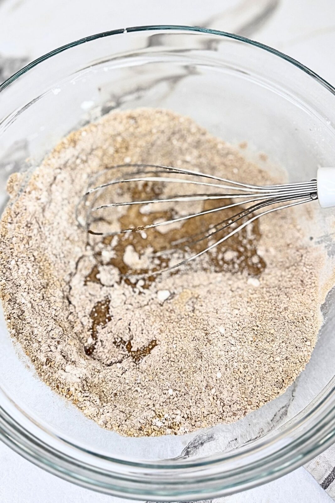 Ground cookies, powdered sugar, and cocoa powder in a glass bowl with a whisk for making chocolate coconut roll.