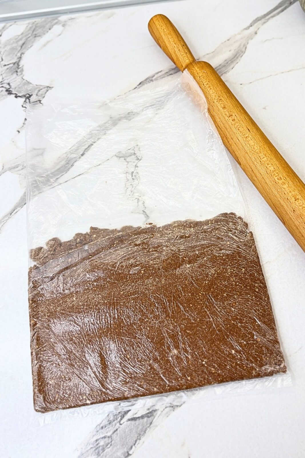 Cocoa cookie dough rolled into an even rectangle inside a freezer bag, with a wooden rolling pin beside it.