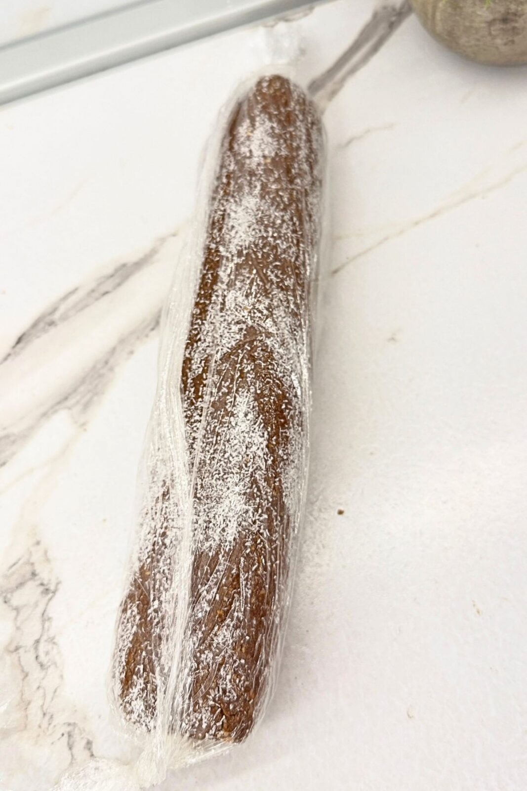 Coconut-coated chocolate coconut roll wrapped in plastic wrap, ready to refrigerate until firm.