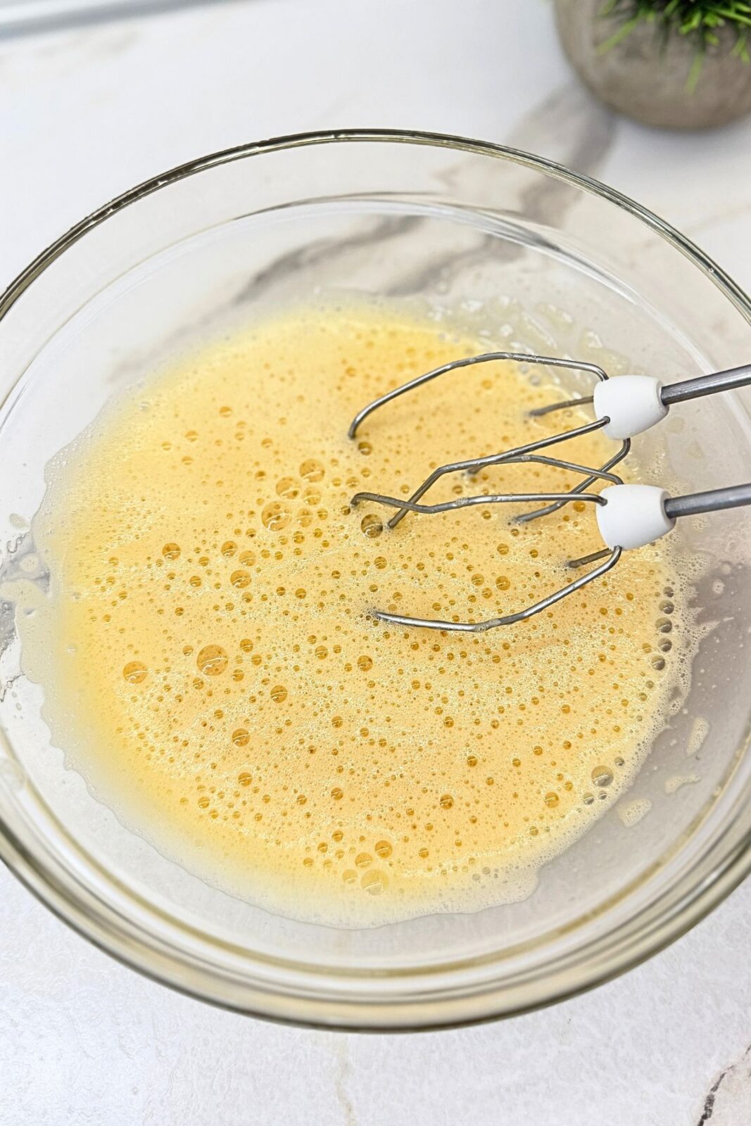 Eggs, sugar, and vanilla beaten together in a glass bowl with a hand mixer.