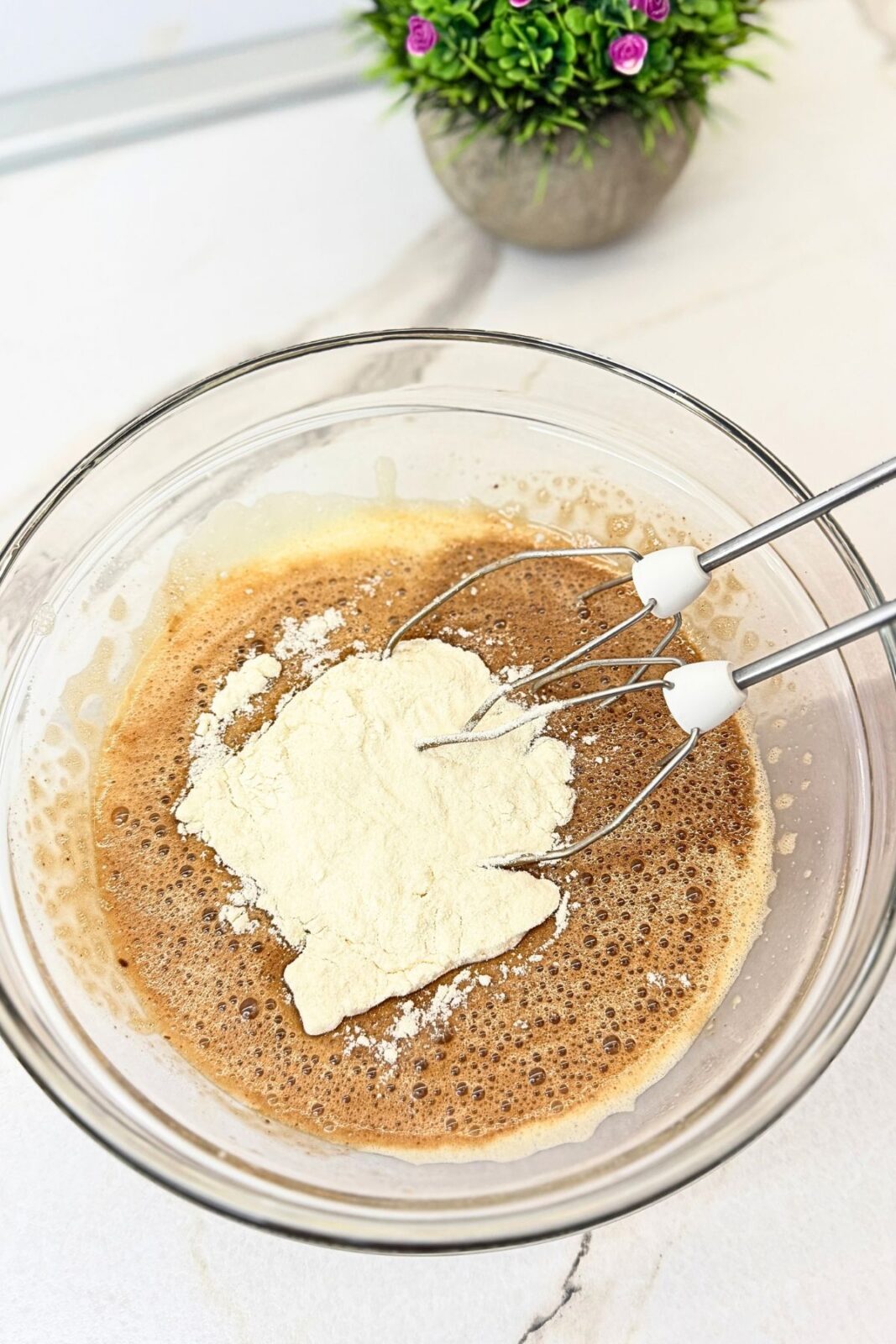 Flour added to the chocolate lava cake batter in a glass mixing bowl.