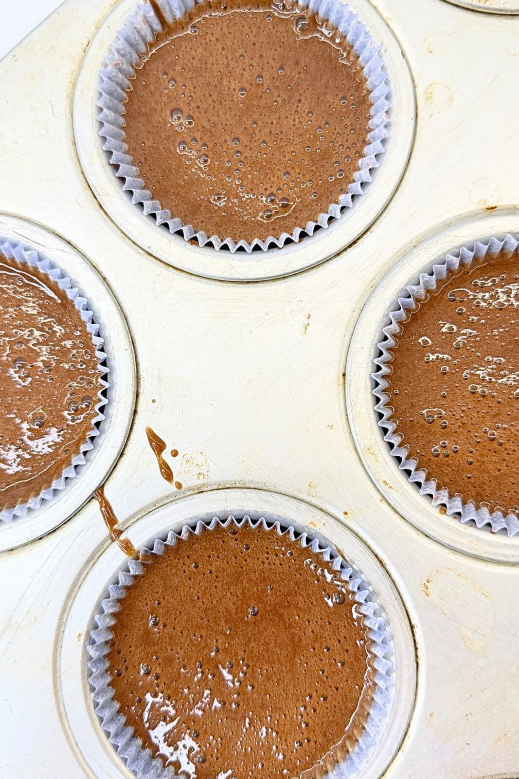Chocolate lava cake batter divided among paper-lined muffin cups before baking.