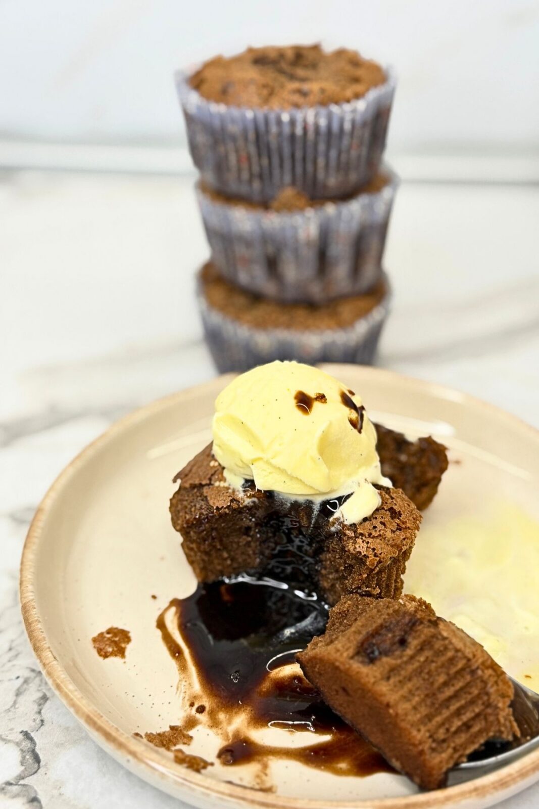 Chocolate lava cake with a molten chocolate center, topped with vanilla ice cream and served with a spoonful of cake on a cream-colored plate.