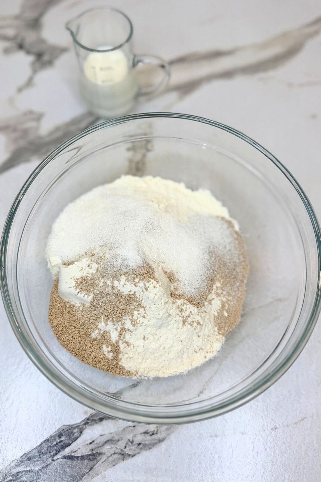 Flour, sugar, and yeast in a glass mixing bowl for making cranberry bread dough.