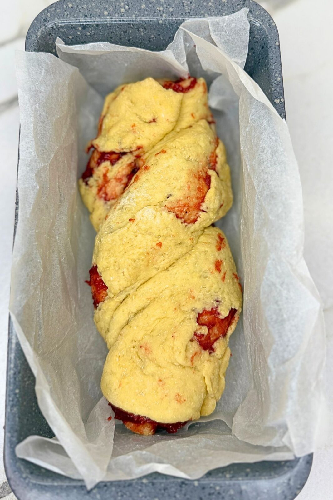 Braided cranberry bread dough in a parchment-lined loaf pan before baking.