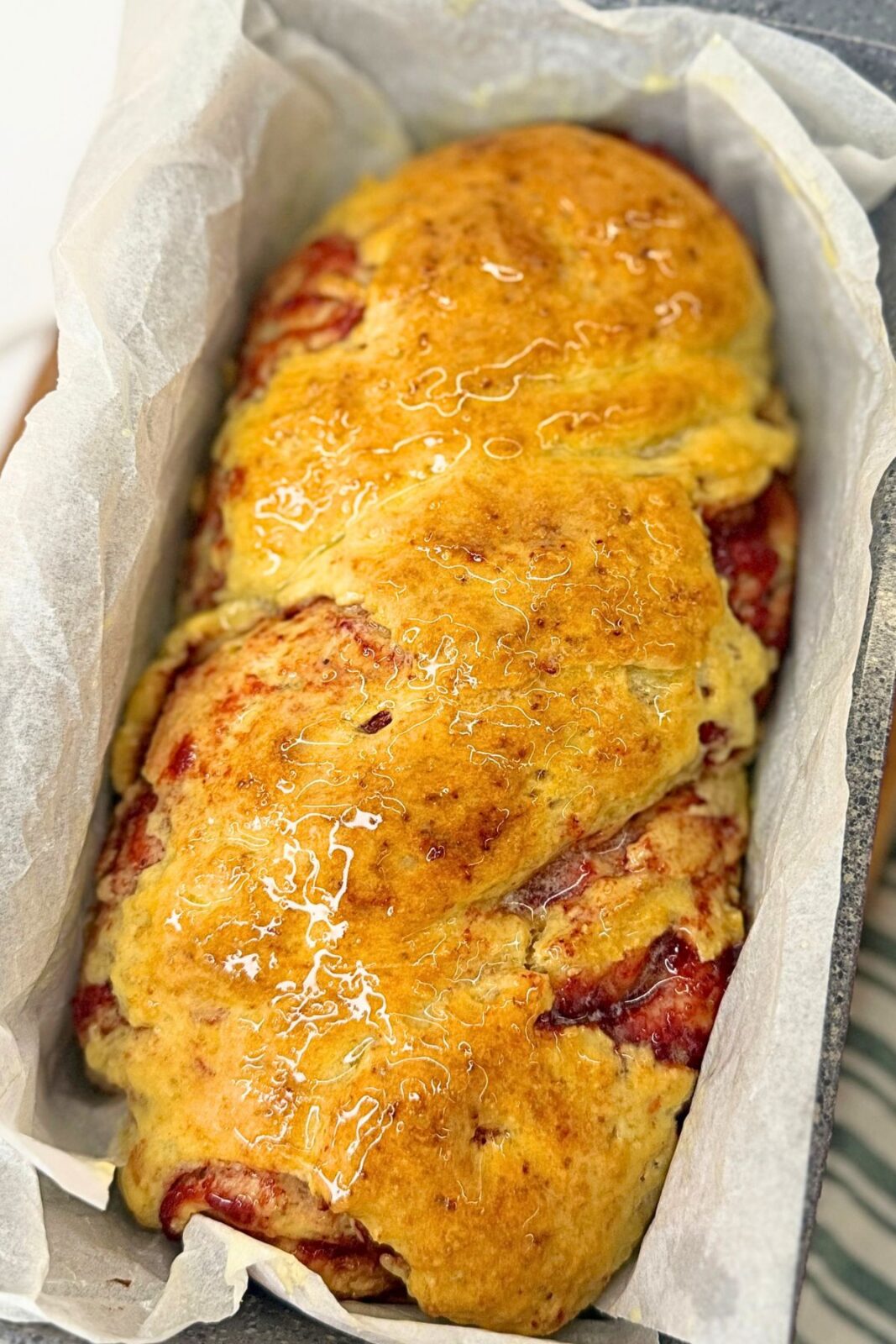 Freshly baked cranberry bread with a golden, buttery crust in a parchment-lined loaf pan.