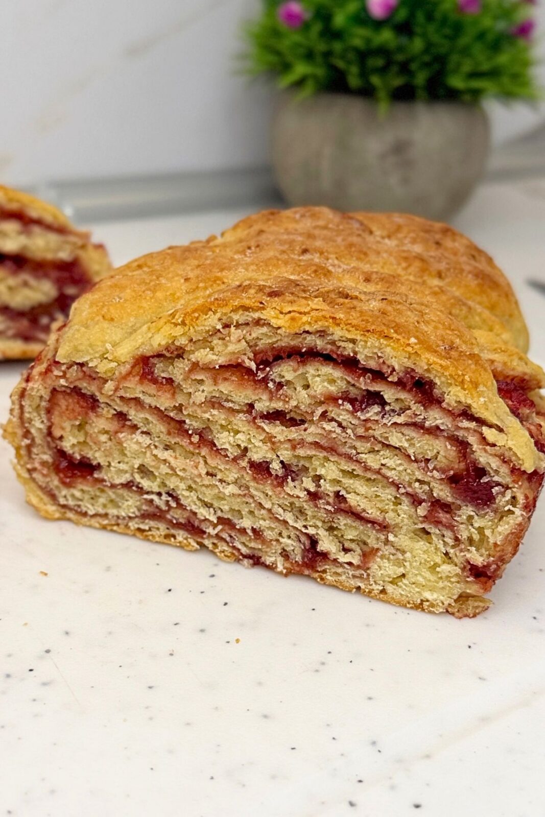 Homemade cranberry bread with a golden crust and layers of cranberry jam, shown cut open on a white board.