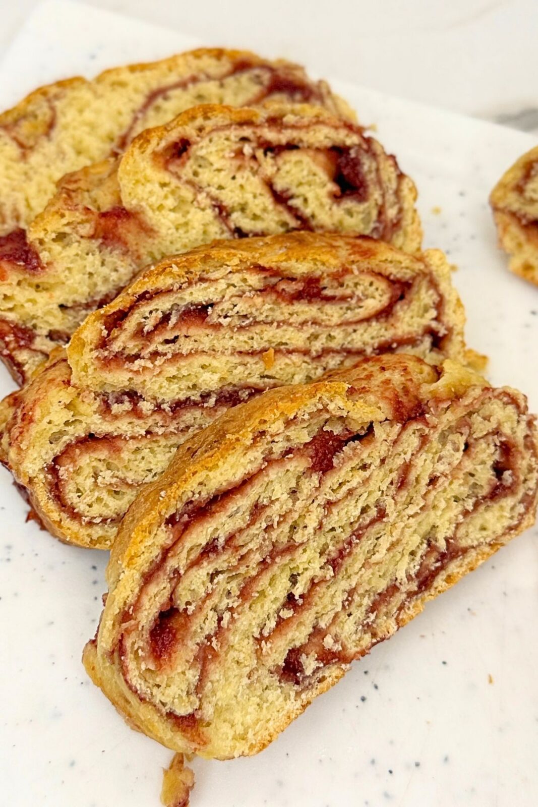 Slices of homemade cranberry bread with cranberry jam swirls and a golden crust on a white board.