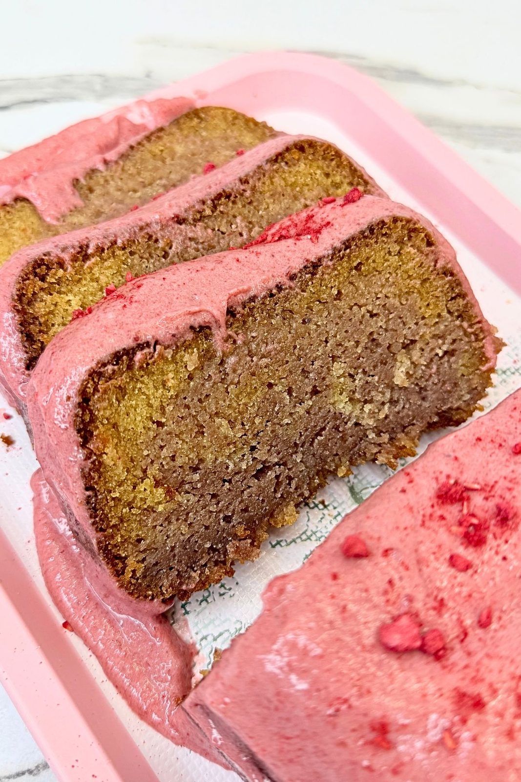 Cranberry loaf cake slices with a marbled vanilla and cranberry crumb, topped with pink cranberry cream cheese glaze on a pink serving tray.