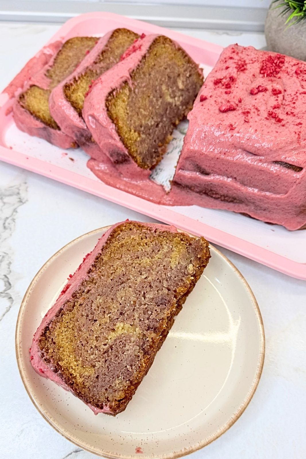 Slice of marbled cranberry loaf cake with pink cranberry cream cheese glaze on a plate, with the remaining sliced loaf behind it.