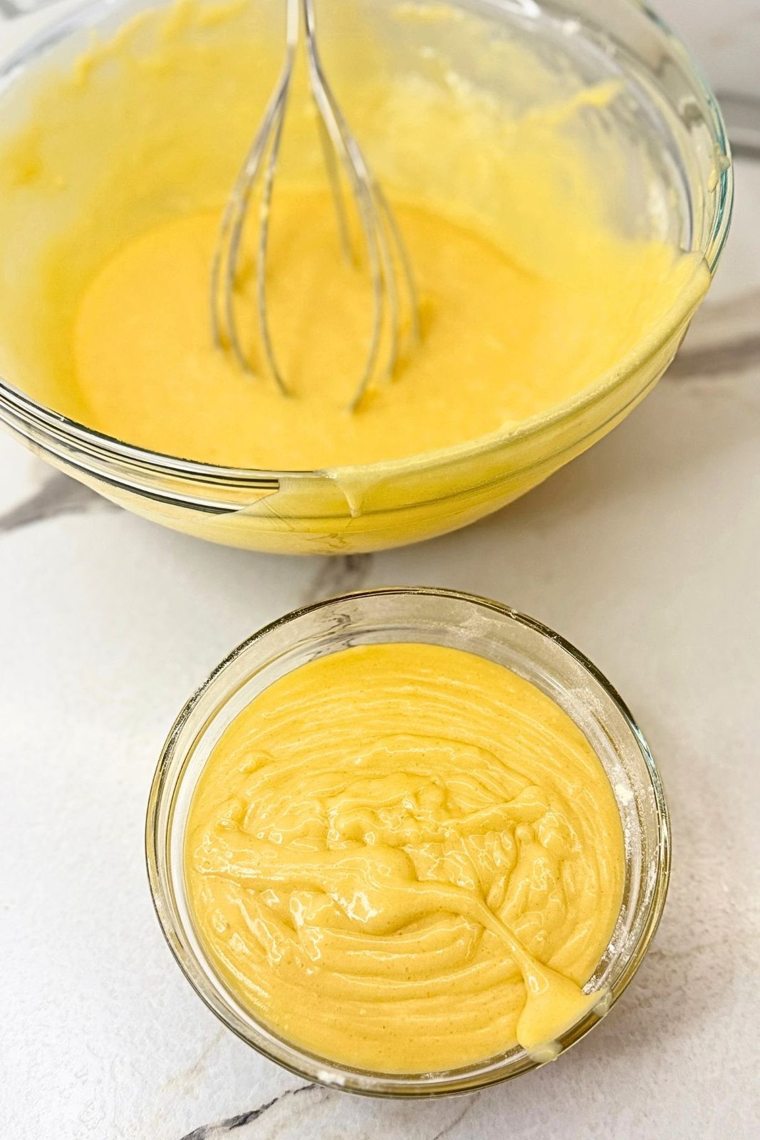 Vanilla cake batter divided between two glass bowls before adding cranberry jam.