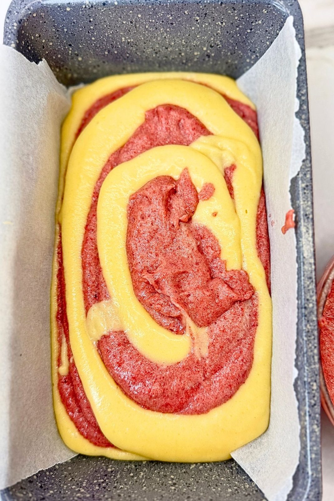 Alternating layers of vanilla and cranberry batter in a parchment-lined loaf pan before baking.
