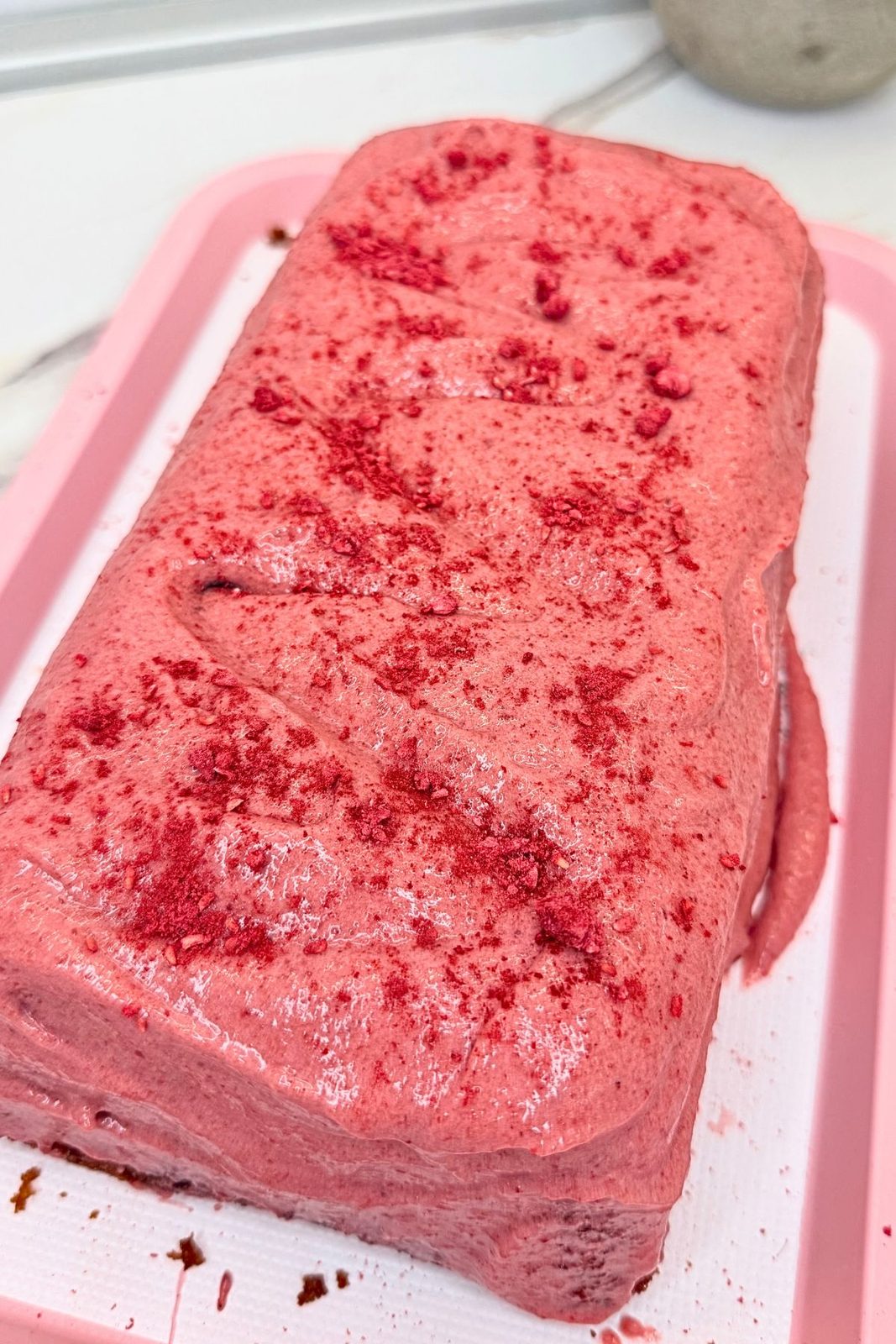 Cranberry loaf cake covered with pink cranberry cream cheese glaze and red crumbs on a pink serving tray.
