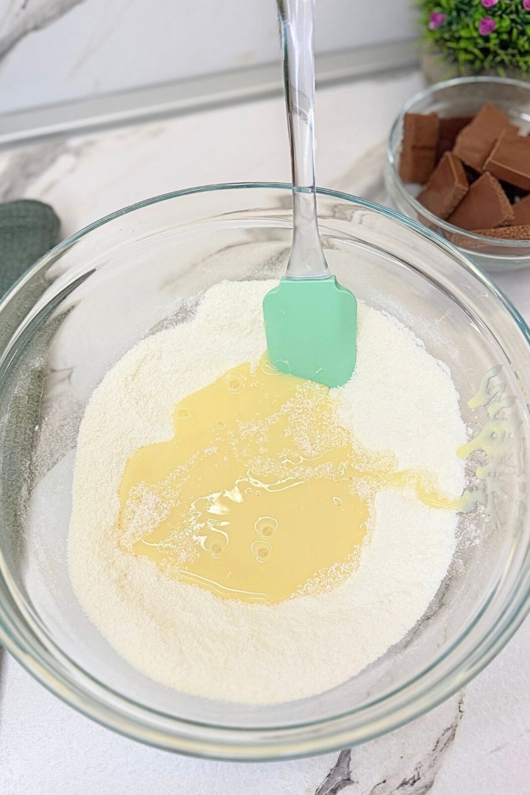 Sweetened condensed milk added to the dry coconut mixture in a glass mixing bowl.