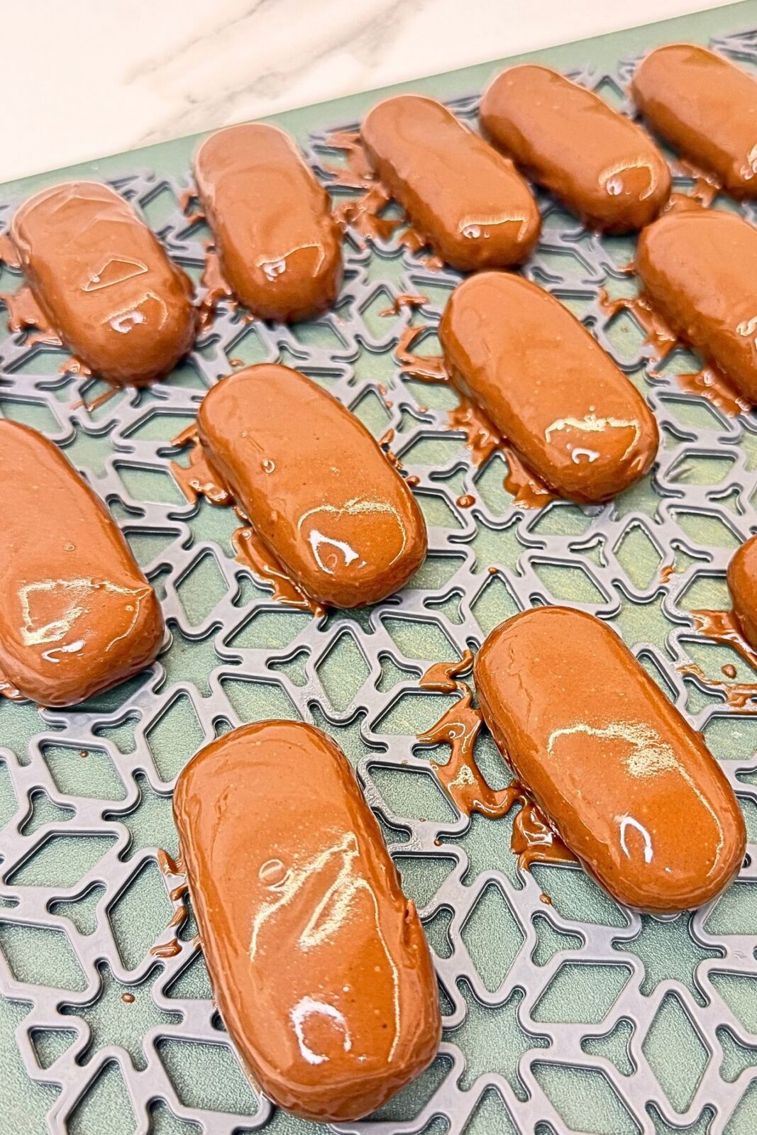 A coconut bar coated in melted milk chocolate held above a saucepan of chocolate.