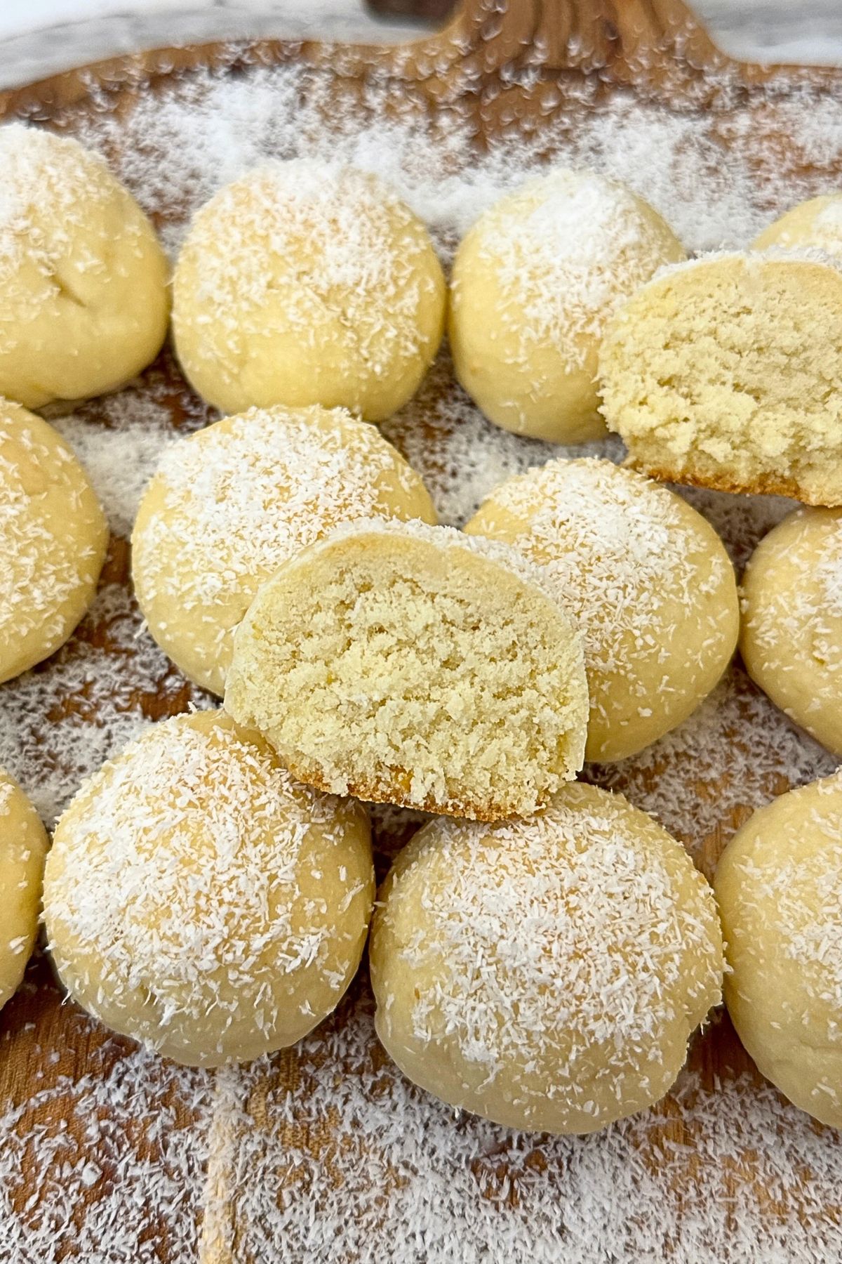 Lemon coconut shortbread cookies topped with lemon glaze and shredded coconut, with a halved cookie showing the crumbly interior.