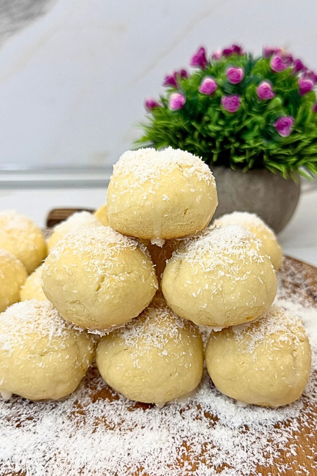 Lemon coconut shortbread cookies stacked on a wooden board, topped with lemon glaze and shredded coconut.