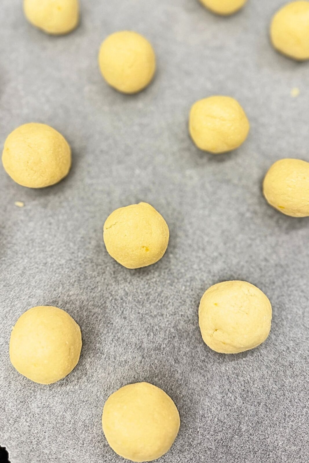 Balls of lemon coconut shortbread cookie dough arranged on a parchment-lined baking sheet.