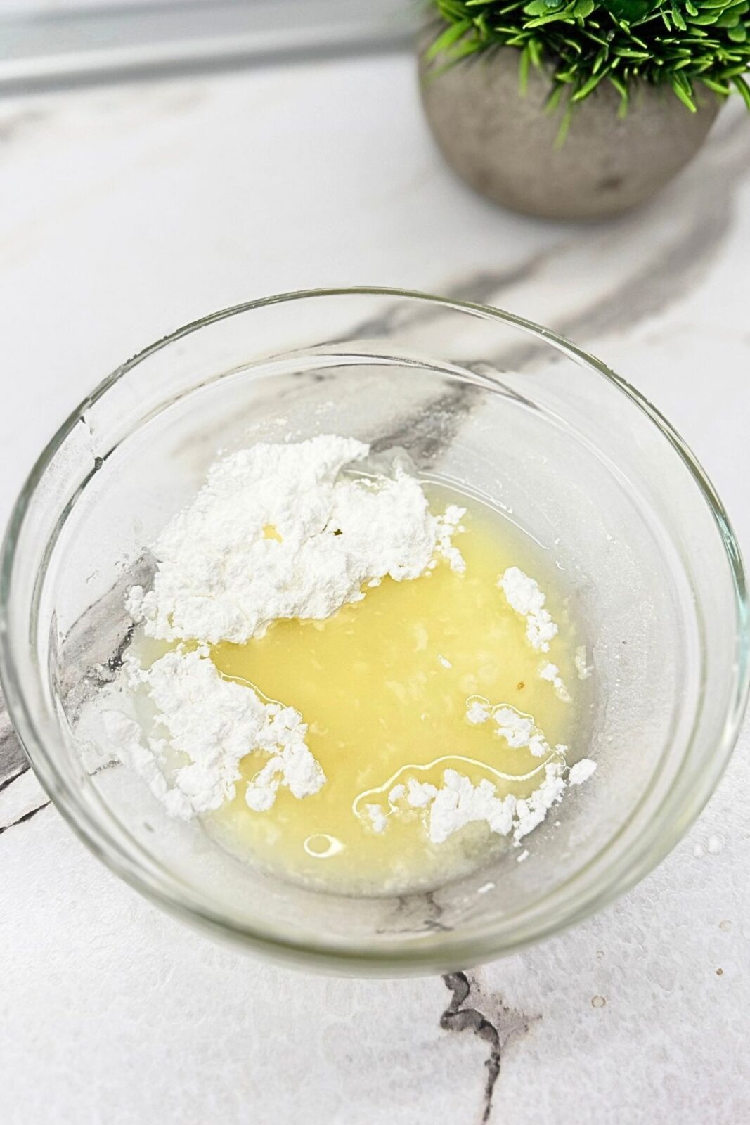 Powdered sugar, lemon juice, and milk in a glass bowl before mixing into lemon glaze.
