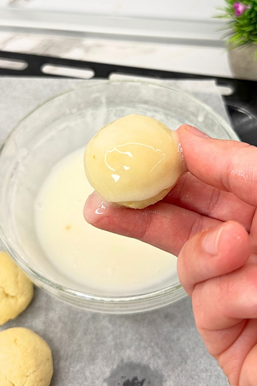 A hand holding a lemon coconut shortbread cookie freshly dipped in lemon glaze.