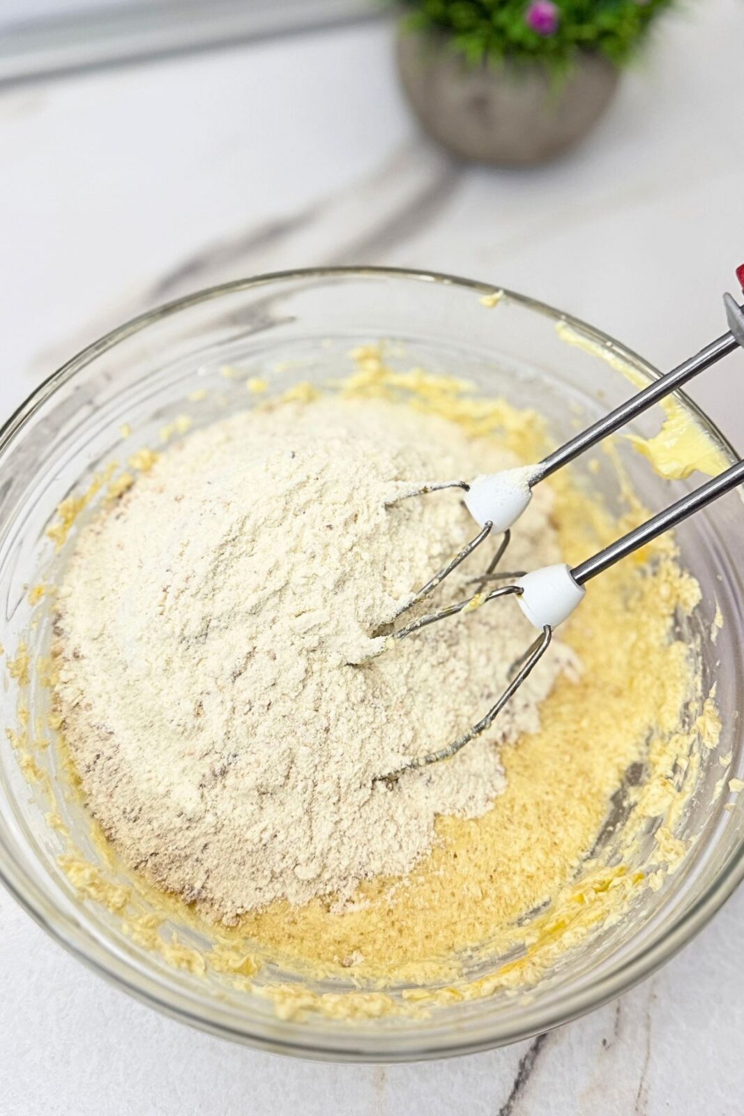 Dry ingredients added to the butter mixture in a glass bowl to make Linzer cookie dough.