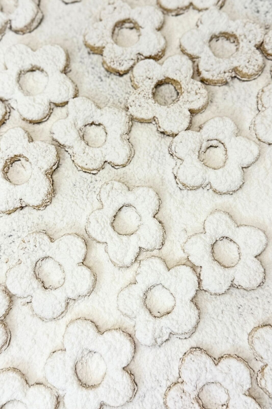 Flower-shaped Linzer cookie tops with center cutouts dusted with powdered sugar.