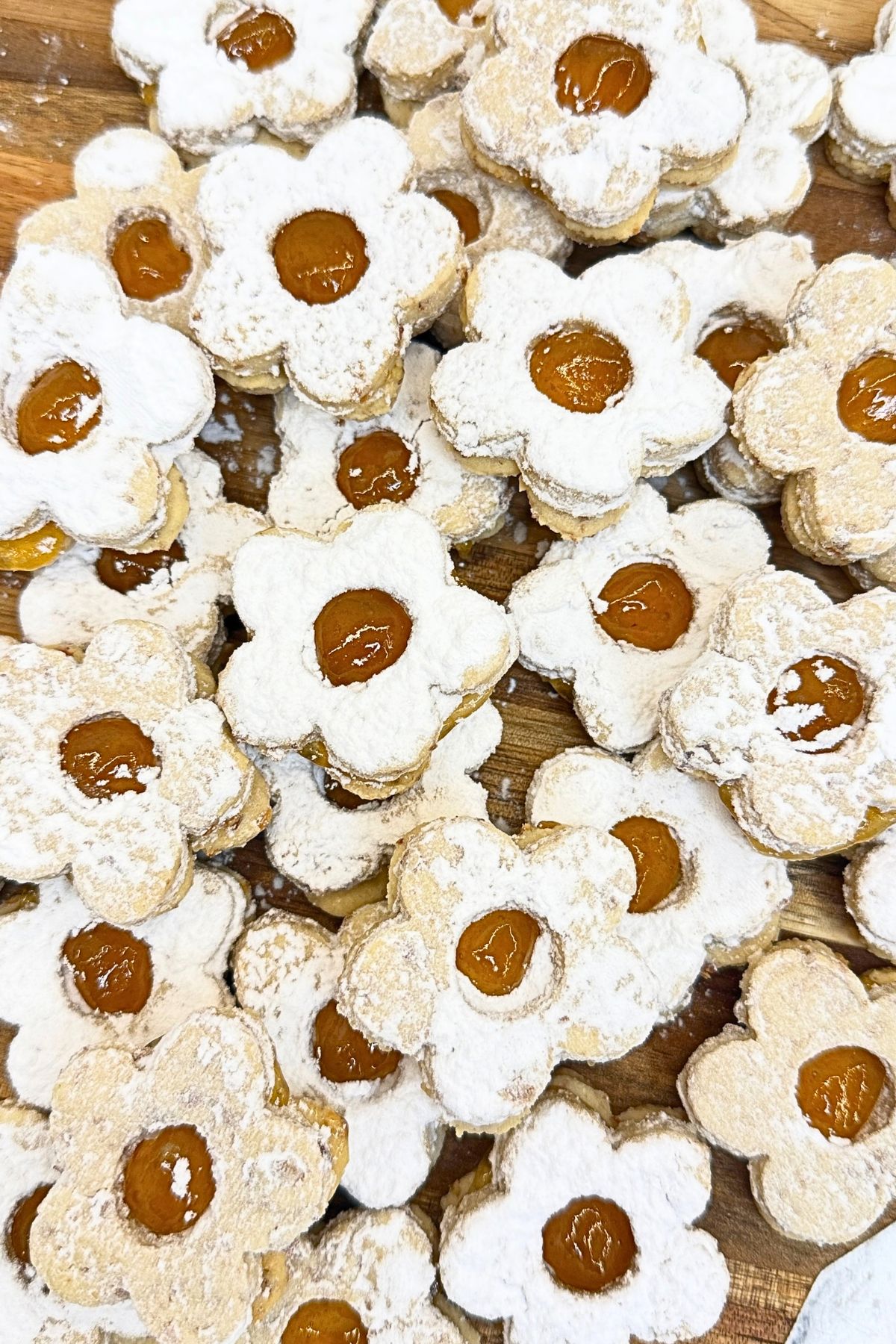 Flower-shaped Linzer cookies filled with apricot jam and dusted with powdered sugar on a wooden serving board.