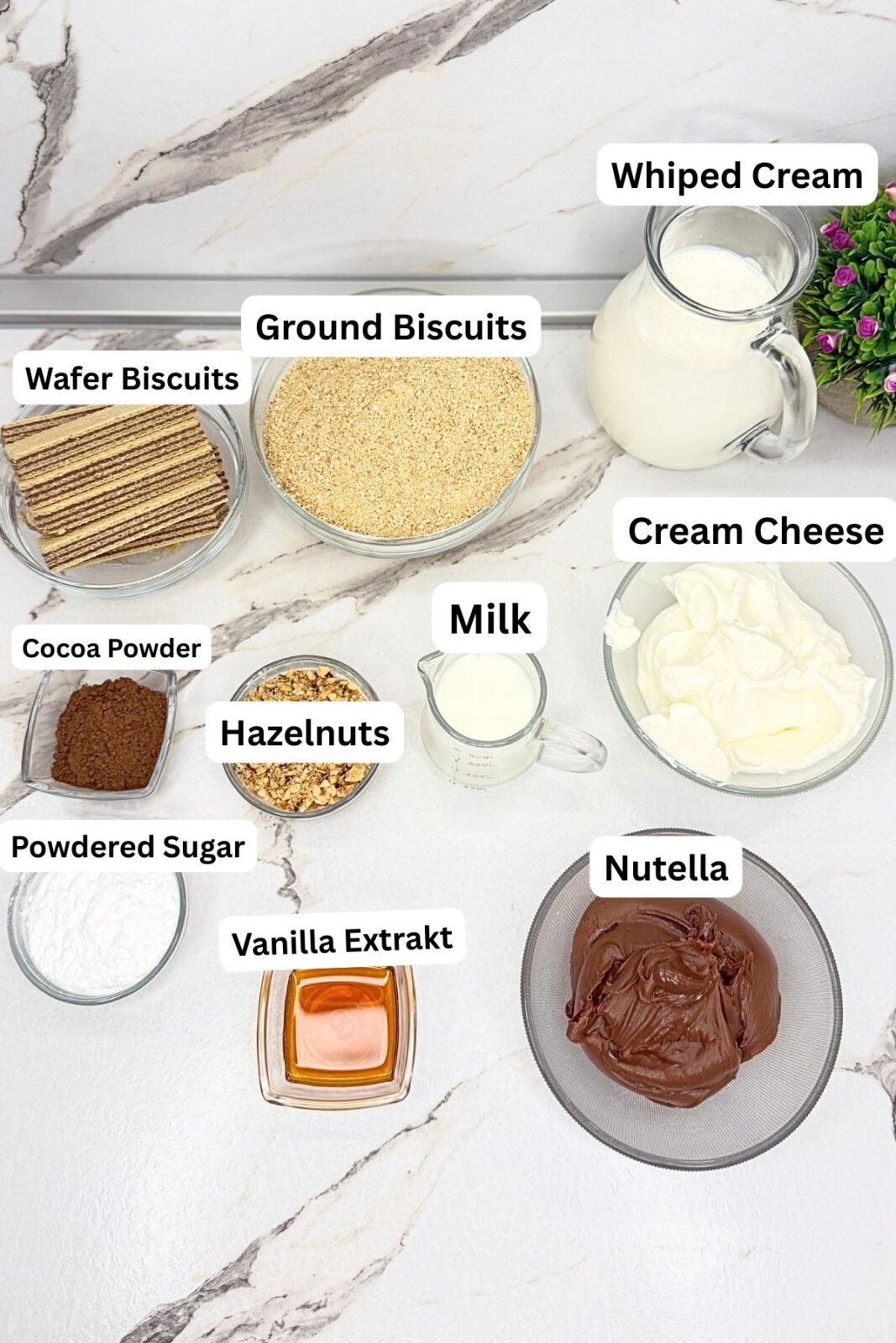 Ingredients for no-bake Ferrero Rocher cake: cookie crumbs, cocoa powder, milk, cream cheese, heavy cream, Nutella, hazelnuts, wafer cookies, powdered sugar, and vanilla extract.