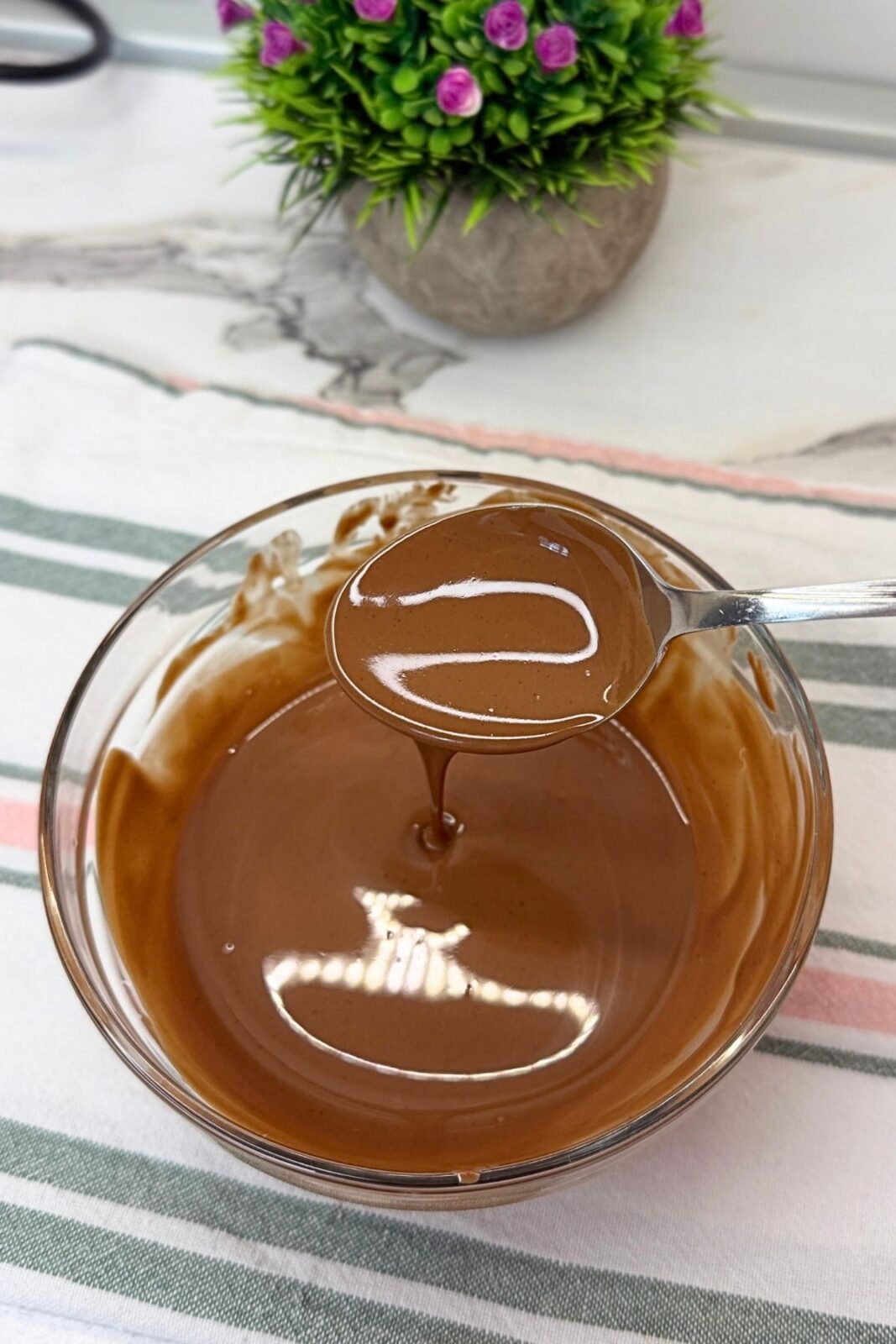Smooth nougat chocolate topping in a glass bowl, ready to pour over the chilled cake.